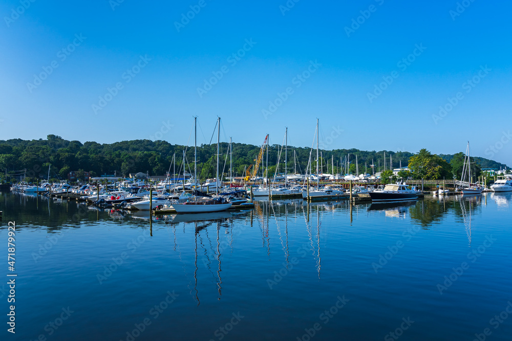 Marina in the Gulf of the Atlantic Ocean early in the morning. Yachts, vessels, ships, and boats large and small are neatly lined up. The blue sky is reflected in the mirror water