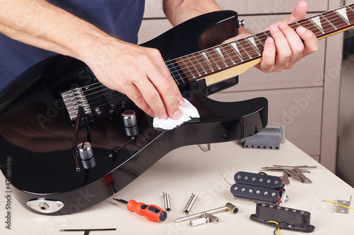 Guitar master wipes surface of modern electric guitar with rag.