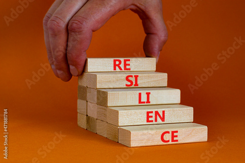 Resilience symbol. Wooden blocks with the word Resilience. Beautiful orange background, copy space. Businessman hand. Business, resilience concept.
