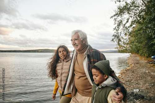 Fotografia Cute biracial girl looking at her grandfather and listening to him during walk a