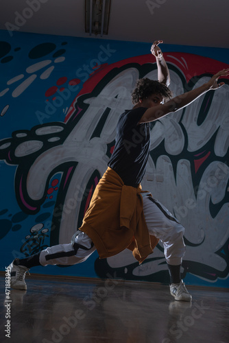 Young black male dancing hip hop style in an urban setting. he is wearing a orange outfit and is on a graffiti background.