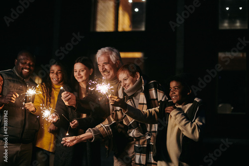 Large happy interracial family of three generations holding sparkling bengal lights while celebrating new year or xmas together