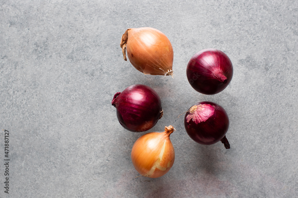 Obraz premium Fresh purple onions outdoors on gray background. Red onion bulb harvested.Copy space. Food levitation concept.