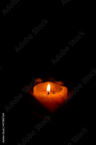 Adult person holding in his hands a thick candle with the light burning in the darkness.
