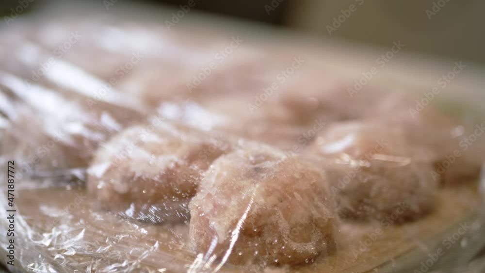 Female Checks the Freezing Process of Ready-Made Semi-Finished Products. Chicken meat meatballs, cutlets covered with ice lie on a wooden board. Deep freezing of preparations. Home kitchen. Close up. Female Checks the Freezing Process of Ready-Made Semi-Finished Products. Chicken meat meatballs, cutlets covered with ice lie on a wooden board. Deep freezing of preparations. Home kitchen. Close up.
