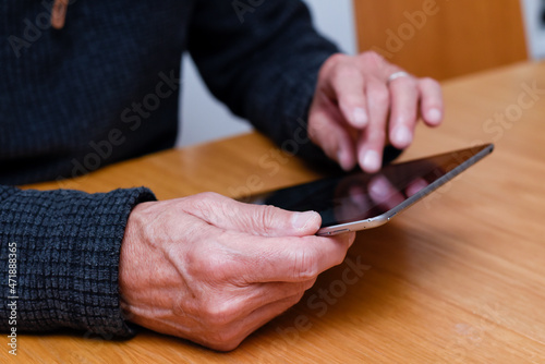 Mature hands hold a touch screen tablet device to stay connect online at home