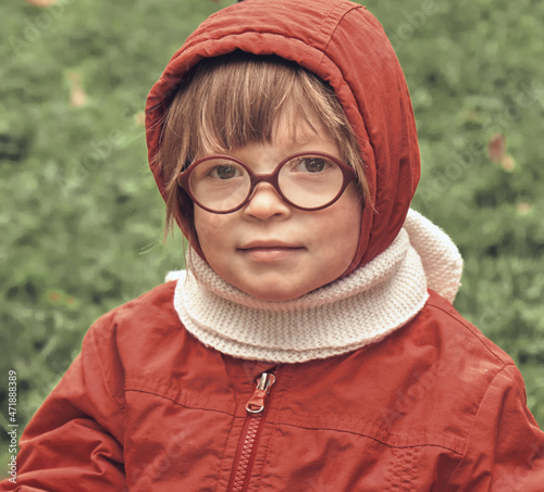 Little girl in a hood and glasses looks at the camera. Close up portrait in retro style
