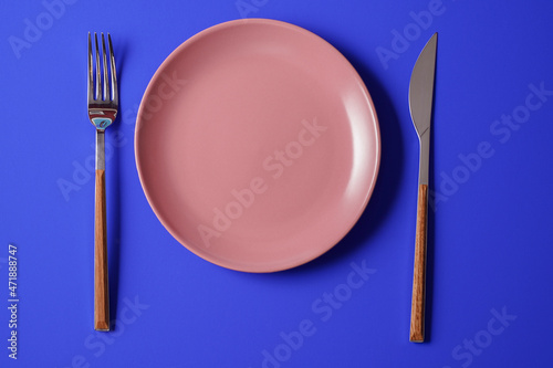 Empty plate and a cutlery set on blue paper background.