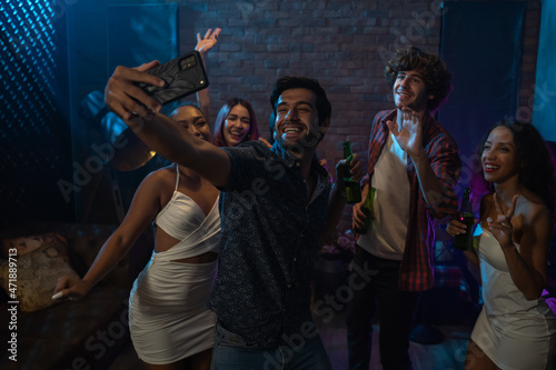 Diverse group of young people dancing at the night club, and taking a selfie with smartphone