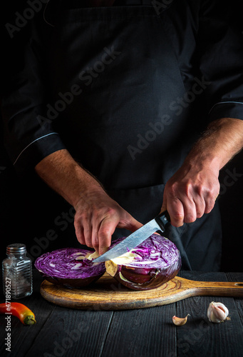 Professional cook is cutting red cabbage with a knife. Cooking vegetable salad in the restaurant kitchen. Vegetable diet idea.