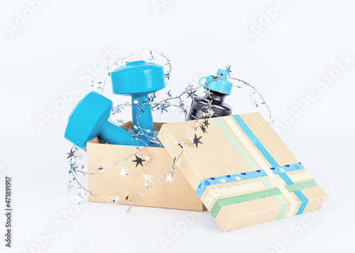 Open gift cardboard box with water bottle, blue dumbbells, shiny silver Christmas decoration on a light background, close-up, front view. Boxing day.