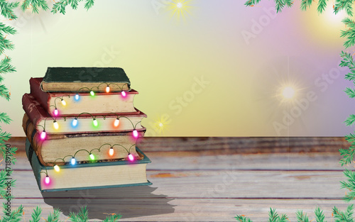 Christmas tree made of books on wooden table on bright background. There are bright and shany lights on background. There are pine ornaments at the corners. There is text area.