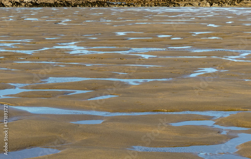 Abstract image of an intertidal sandy beach after an ebb tide. with saltwater pools and sand formations caused by receding waters. Reflections of blue sky in the standing puddles. Landscape, Bude, UK. photo