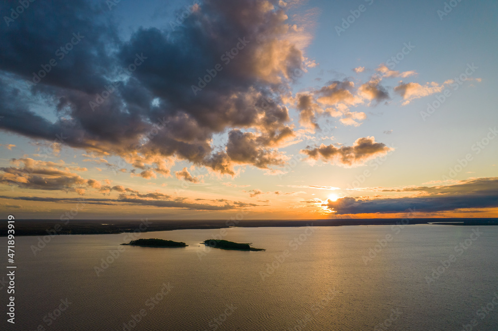 Sunset over the lake. Blue sky and orange sun during summer sundown. Small islands in the distance.