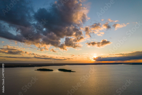 Fototapeta Naklejka Na Ścianę i Meble -  Sunset over the lake. Blue sky and orange sun during summer sundown. Small islands in the distance.
