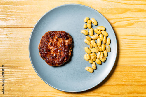 Tasty grilled burger served with coocked vegetarian beans in a plate on a rustic wooden table. Flat lay, top view photo