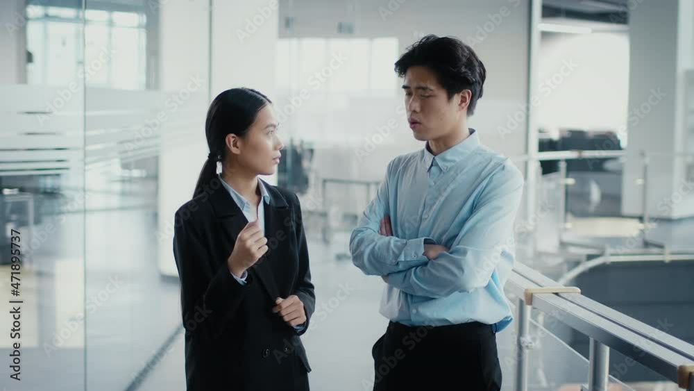 Two Asian Coworkers Talking Discussing Work Standing In Modern Office Two Asian Coworkers Talking Discussing Work Standing In Modern Office
