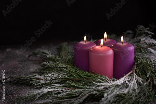 Christmas wreath with four burning purple advent candles.