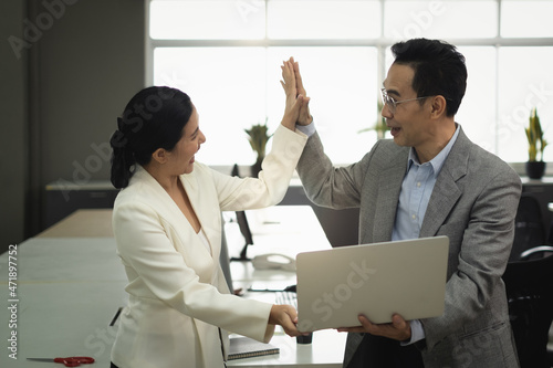Office employees Asian women holding laptop together discuss with manager her about job project complete with perfect and do high five