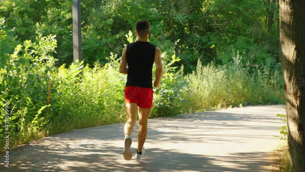 Slow motion fit man wearing shorts and top running on road curve in