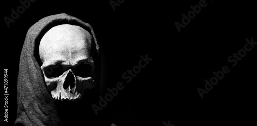 Human skull in hood close up on black background. Free space photo