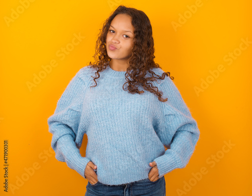 Portrait of lovely funny Teenager girl wearing blue sweater over yellow background sending air kiss