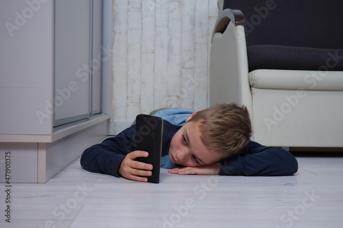 młody chłopiec leży na podłodze patrzy w telefon