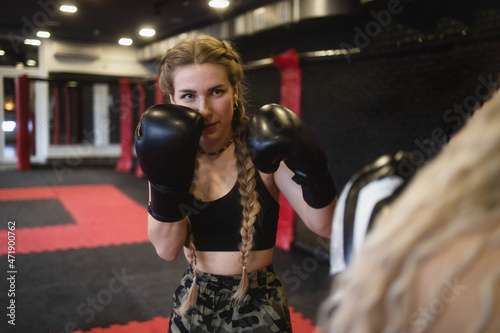 Two young women in boxing gloves perform sparring, view from the side of one of the athletes. Women's fitness boxing workout in the gym