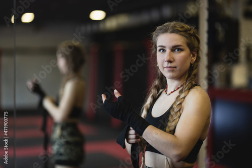 A young woman with braids prepares for a workout, she wraps a tight bandage around her hands to protect them during  fitness boxing workout in the gym