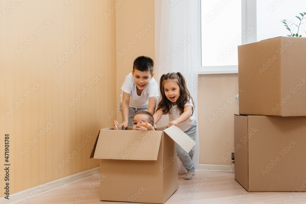 A friendly family of children boys and girls play and roll around each other in a cardboard box, rejoice at moving to a new apartment against the background of cardboard boxes.Transportation of goods. A friendly family of children boys and girls play and roll around each other in a cardboard box, rejoice at moving to a new apartment against the background of cardboard boxes.Transportation of goods.
