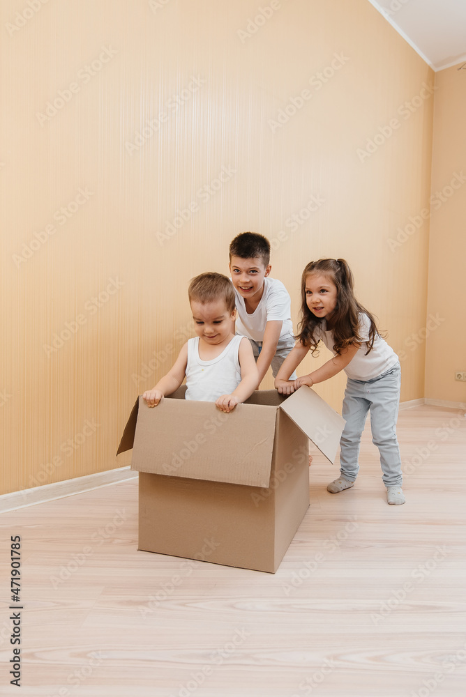 A friendly family of children boys and girls play and roll around each other in a cardboard box, rejoice at moving to a new apartment against the background of cardboard boxes.Transportation of goods. A friendly family of children boys and girls play and roll around each other in a cardboard box, rejoice at moving to a new apartment against the background of cardboard boxes.Transportation of goods.