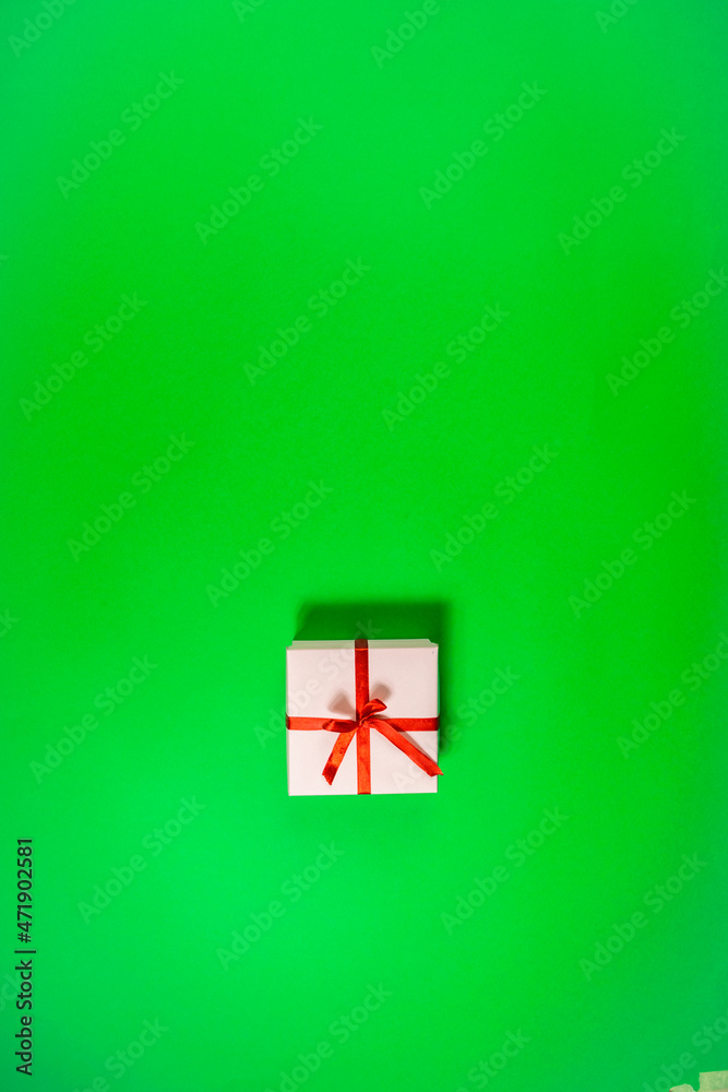 One holiday pink gift box tied with red ribbon on green background.