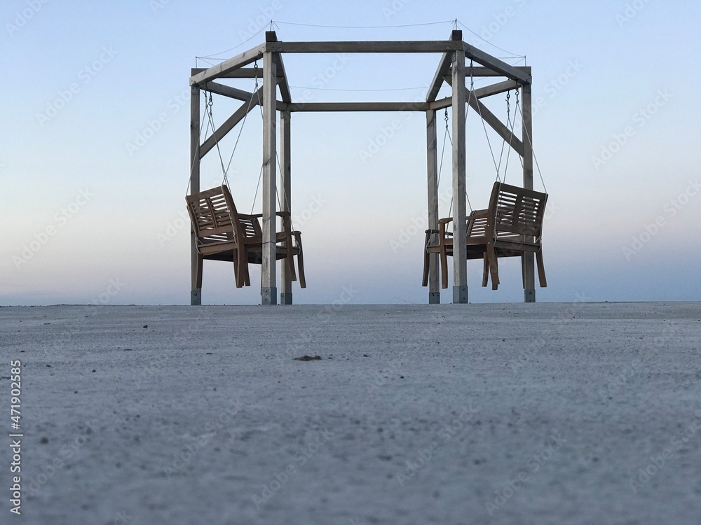 Scenic view of outdoor hexagonal prism with four wood swing rocking chairs on the paved pier of Baltic Sea at dusk Scenic view of outdoor hexagonal prism with four wood swing rocking chairs on the paved pier of Baltic Sea at dusk