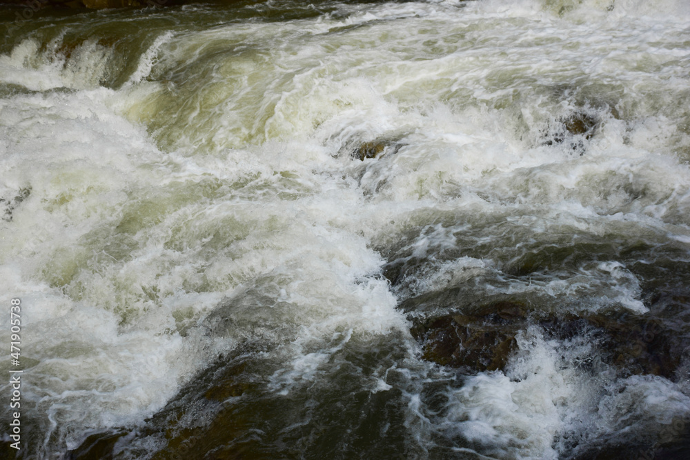 A stormy stream of rushing foamy water on the cascade of the waterfall A stormy stream of rushing foamy water on the cascade of the waterfall