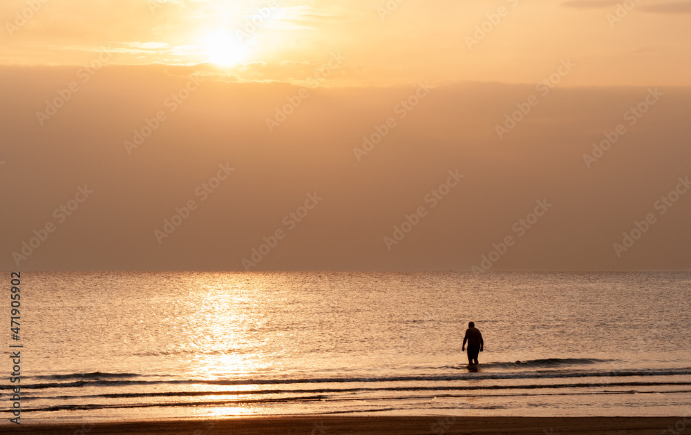 Silhouette of a man in the sea at sunrise. Unrecognized person entering the ocean for swimming in the morning.