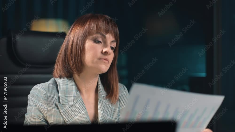 A beautiful girl took a paper document from the table with a schedule of the monthly profit of the enterprise and carefully studies it. A business woman works remotely in a home office. A beautiful girl took a paper document from the table with a schedule of the monthly profit of the enterprise and carefully studies it. A business woman works remotely in a home office.