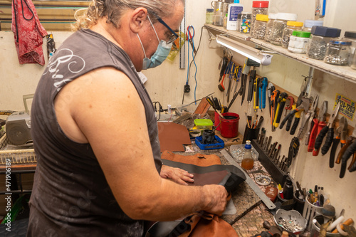 Close up of a latin old man sewing a leather bag. A saddler making design for a new shoes at his workshop. Genuine leather handbag master at work in local workshop. Handmade concept. photo