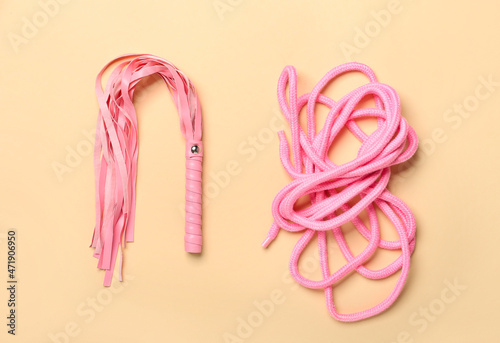 Whip and rope from sex shop on color background