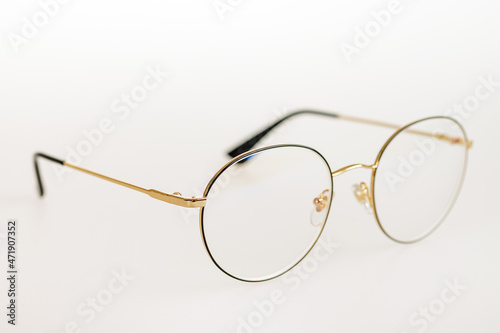 Thin round metal frame of golden-colored glasses, selective focus, close-up