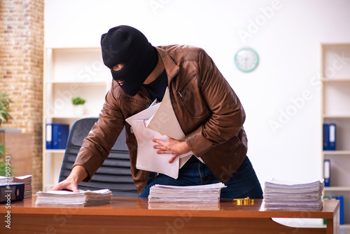 Young man in balaclava stealing information from the office