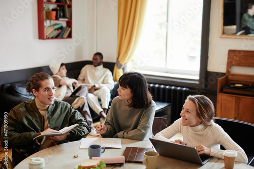 Group of students sitting at the table with laptop and books and preparing for the exam together in the room