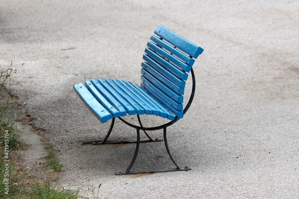 Freshly painted blue wooden boards on top of vintage retro black metal frame public bench mounted on paved sidewalk next to uncut grass at local public park on warm spring day Freshly painted blue wooden boards on top of vintage retro black metal frame public bench mounted on paved sidewalk next to uncut grass at local public park on warm spring day