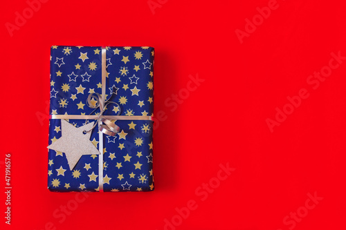 close up festive gift box blue and silver colors with paper christmas star decoration on red background with copy space