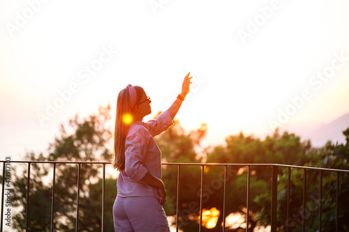 A beautiful woman at sunset stands on a terrace overlooking the sea.