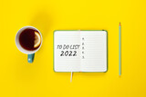 To do list 2022 concept. Mint color Tea cup and notebook with to do list on bright yellow desk from above, planning and design concept. Top view, flat lay, banner with copy space. Mock up.