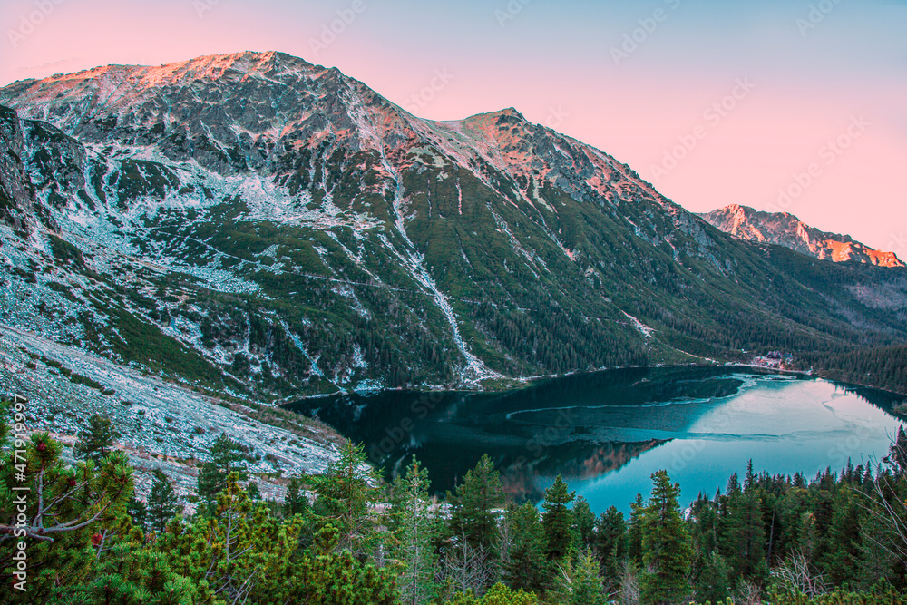 Beautiful turquoise mountain lake in pink lights of sunset or sunrise. Winter time and snow. 