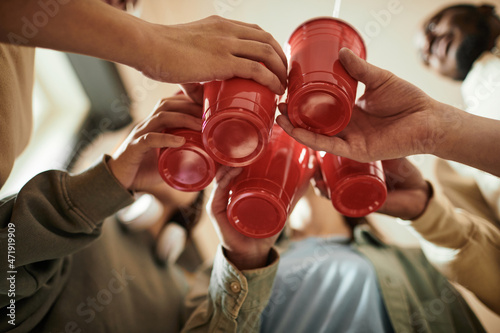 Canvas Print Low angle view of group of teenagers toasting with plastic cups and drinking coc