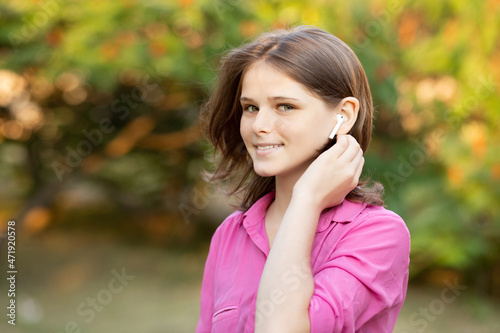 Beautiful young girl enjoy listening to music with wireless headphone with good mood and relax outdoor. 