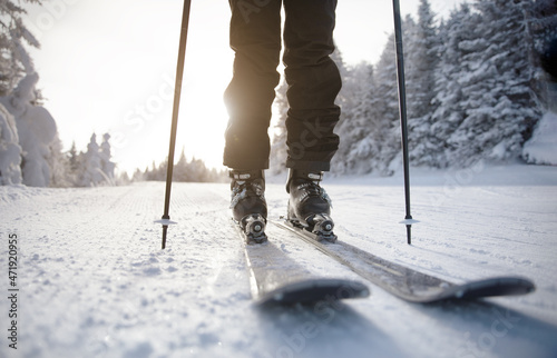 Skiing. Ski on First Tracks. Alpine skier going downhill skiing in morning on Fresh Tracks on groomed ski trail slope piste. Closeup of trail, skis and ski boots amongst snow covered trees