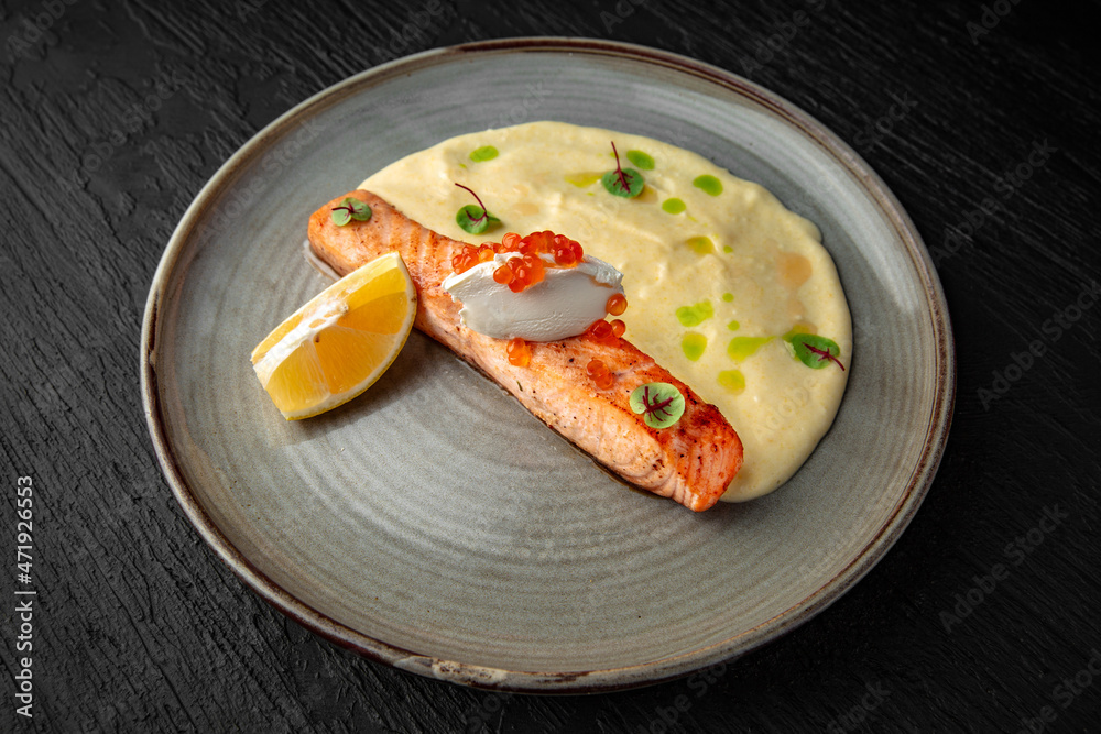 Salmon fillet with mascarpone, red caviar and tender puree in a ceramic plate on a dark textured background. Restaurant menu Isolated on black Salmon fillet with mascarpone, red caviar and tender puree in a ceramic plate on a dark textured background. Restaurant menu Isolated on black